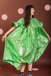 A woman modeling a voluminous, crinkled metallic green dress against a brown backdrop with pink polka dots.